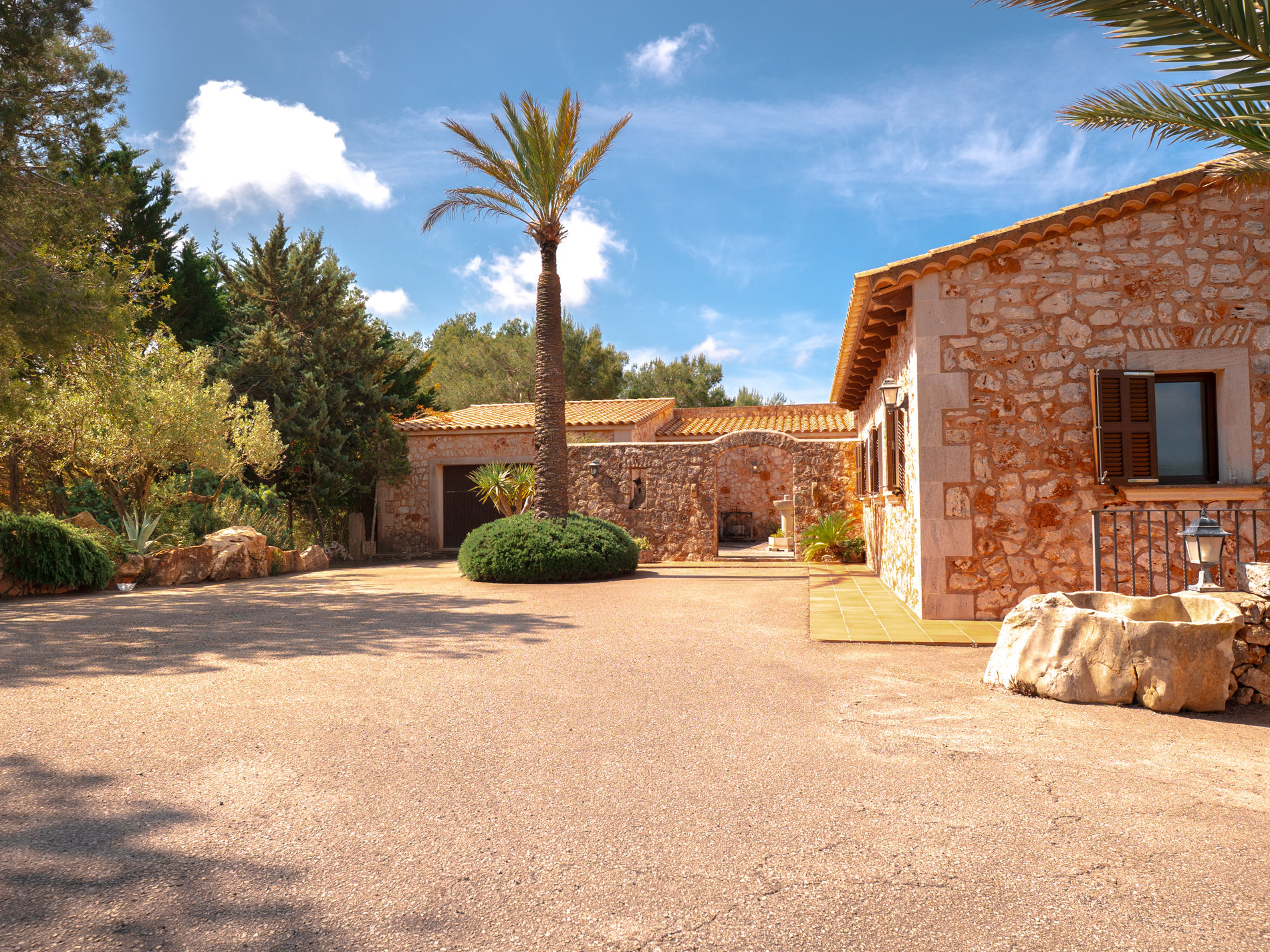 Vorplatz der Finca mit hoher Palme und Natursteinfassade